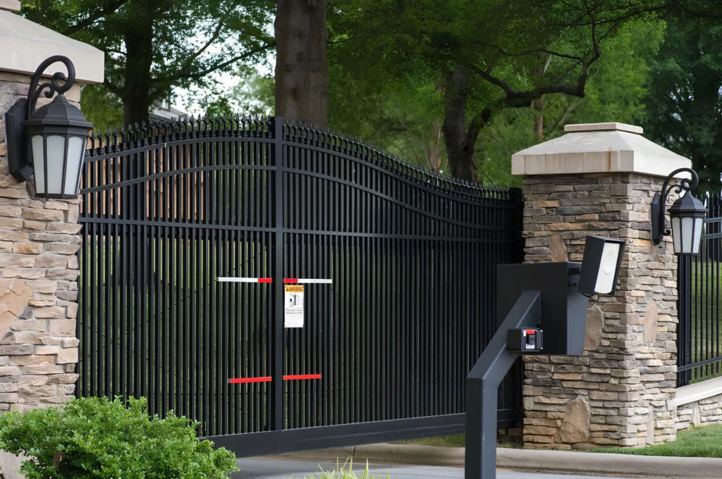 Black metal driveway security gates with stone pillars and electronic access system.