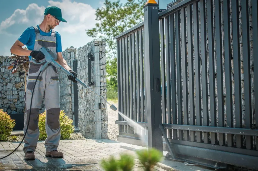 A worker cleaning a residential gate using a pressure washer as part of Residential Gate Repair.