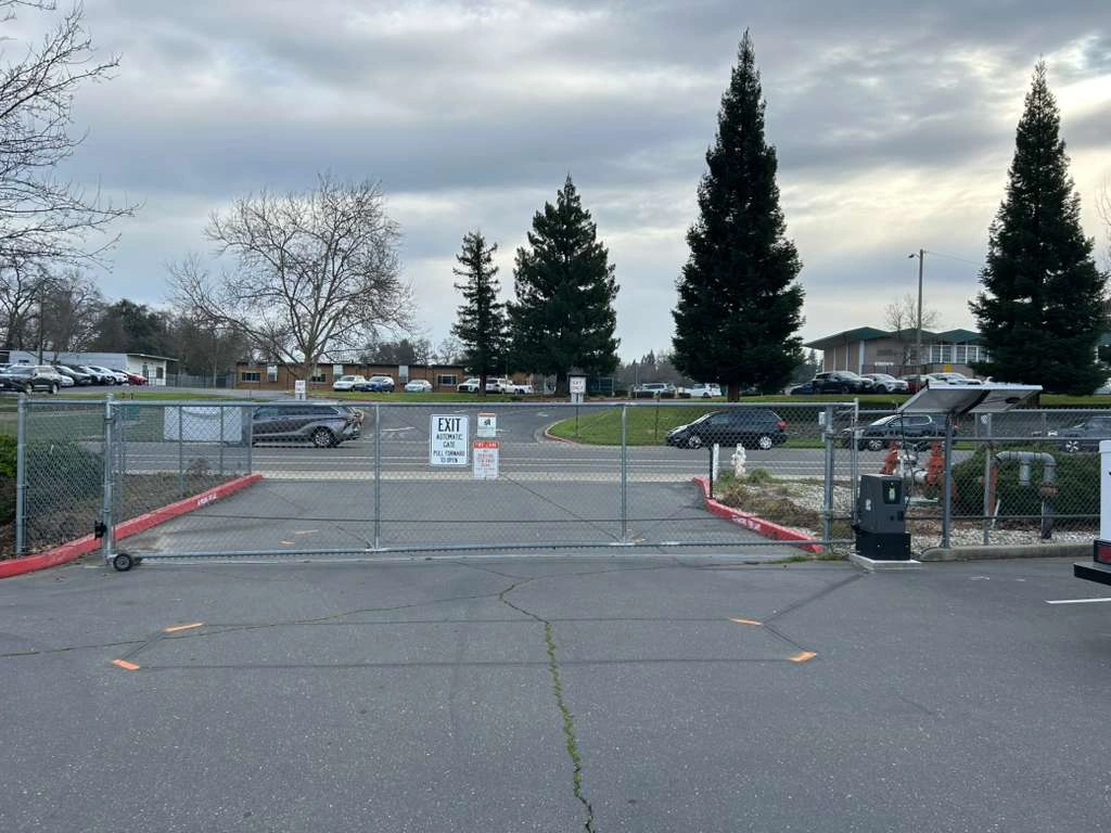 Closed chain link commercial slide gate Sacramento with an automatic exit sign on an asphalt driveway.