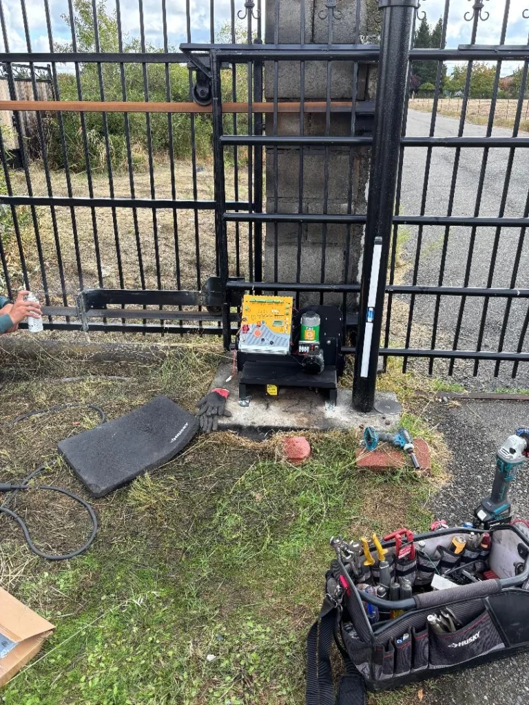 A technician prepares tools and parts for a new gate operator replacement on an automatic sliding metal gate.