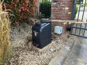 A dark gray LiftMaster automatic gate opener installed near a brick pillar, highlighting LiftMaster vs DoorKing gate operators.