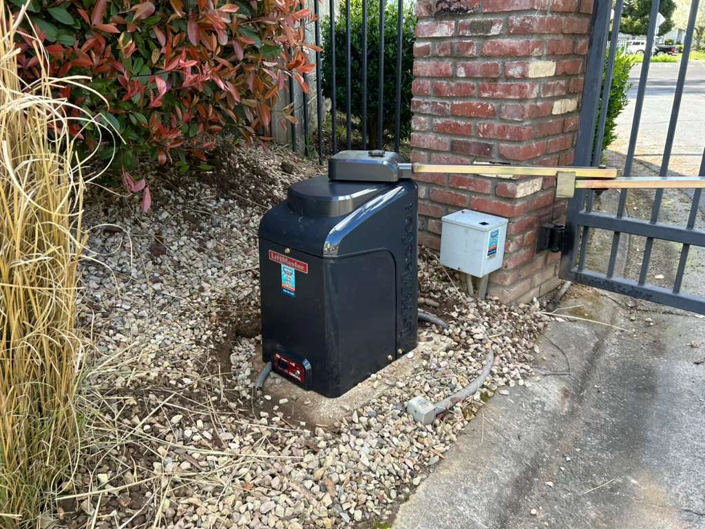 A dark gray LiftMaster automatic gate opener installed near a brick pillar, highlighting LiftMaster vs DoorKing gate operators.