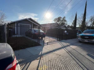 Black iron property security gates Sacramento protecting a residential driveway with parked cars on a sunny day.