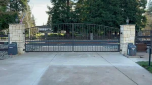 Wrought iron automatic gates Placer County installed on a concrete driveway between stone pillars.